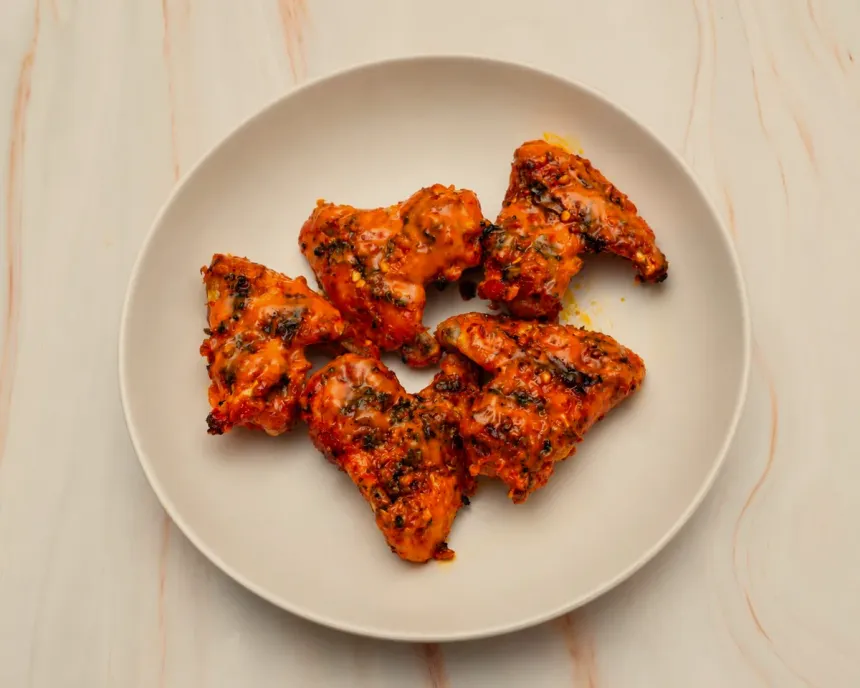Five peri peri wings on a plate, sauced and flecked with herbs